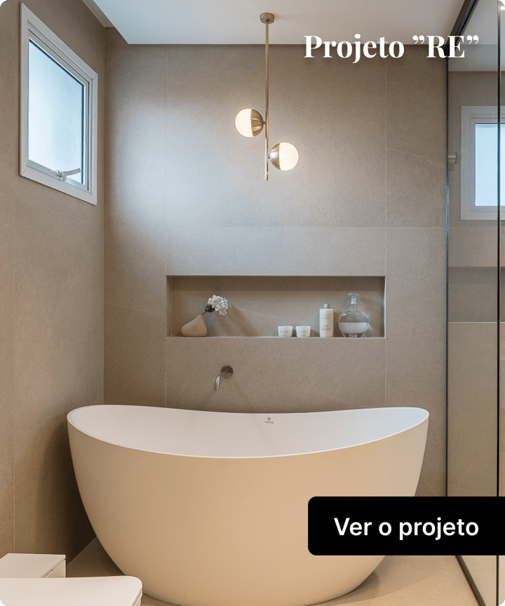 Um box de um banheiro com uma banheira de imersão com formato orgânico branca de meio-círculo, iluminação com luminária pendente, um espaço na parede com cosméticos e uma flor e uma janela à esquerda. Clique para ver projeto